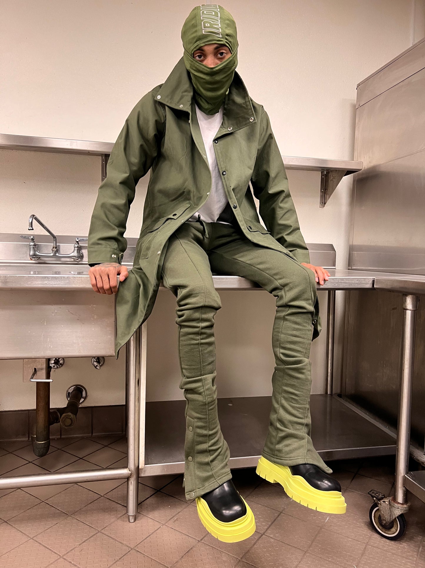 Seated model wearing Green Stacked Joggers and matching olive outerwear