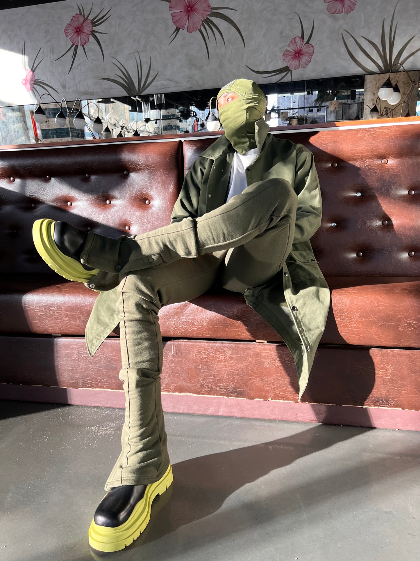 Model seated in a booth wearing Green Stacked Joggers with one leg crossed